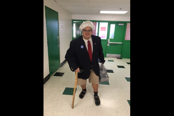 Teacher dressed as an old man walking with a cane and a bag through the hallway