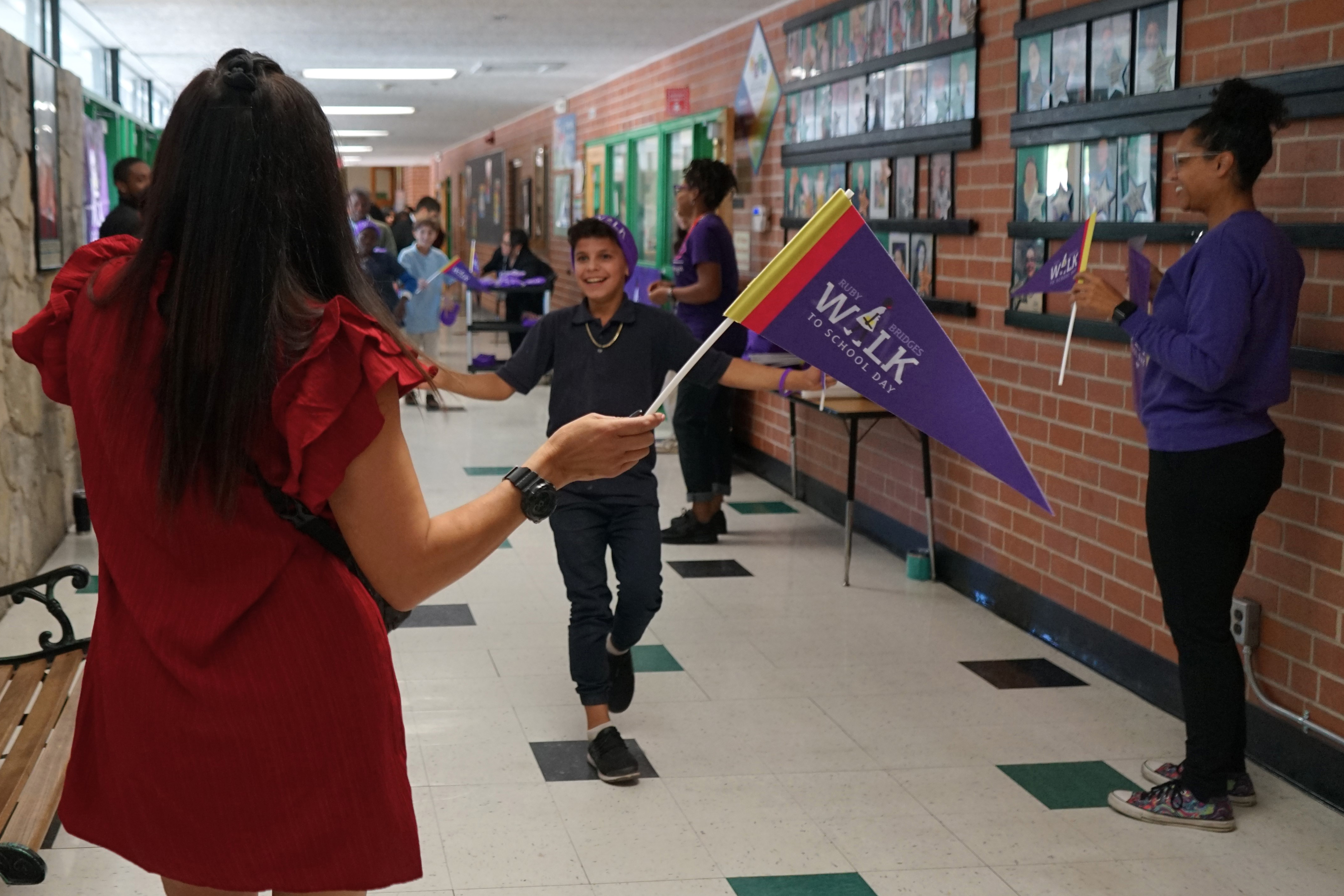 A woman in a red dress waves a purple flag as a boy in a purple beanie walks towards her