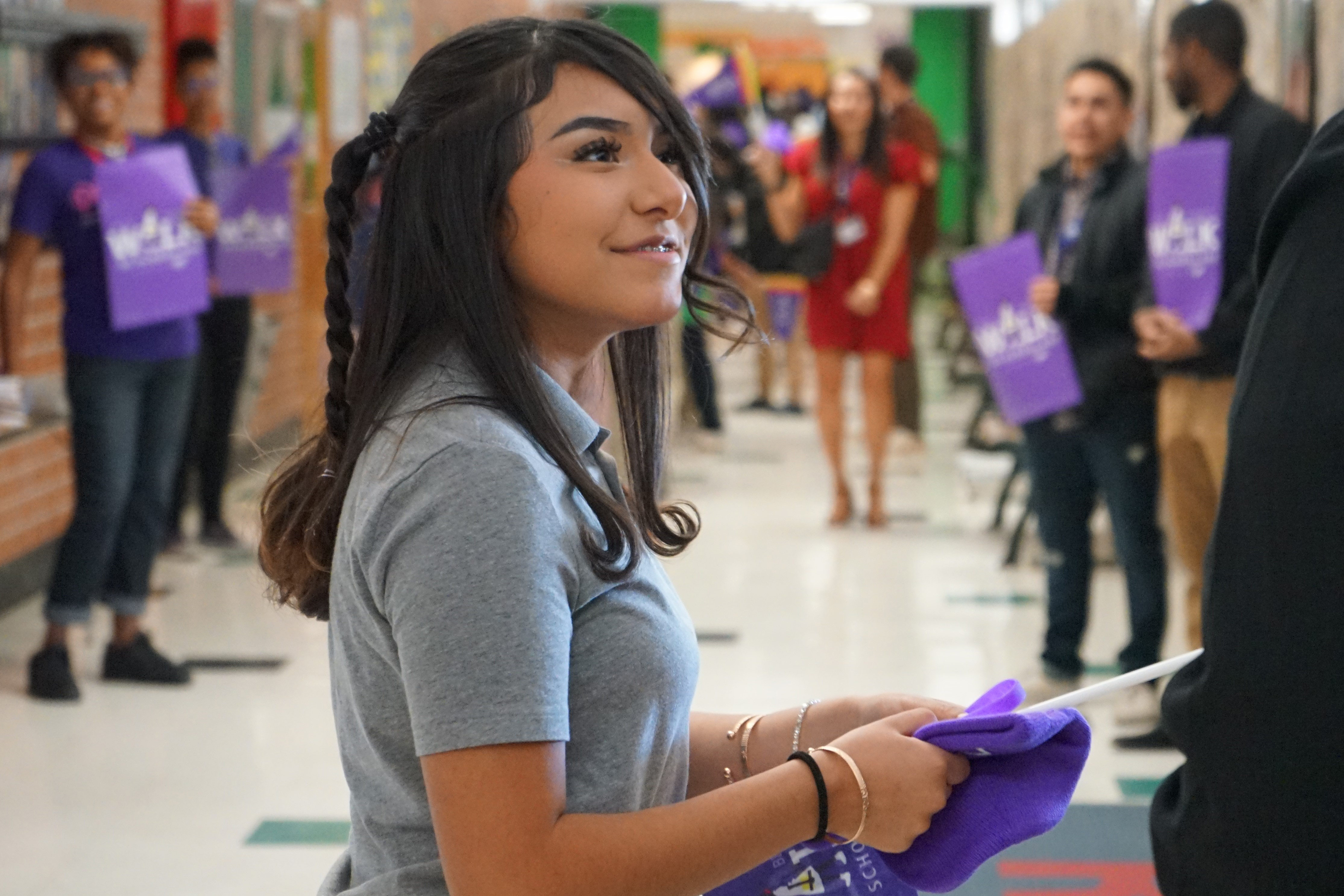 A girl in a grey shirt smiles with a purple beanie and flag in her hands