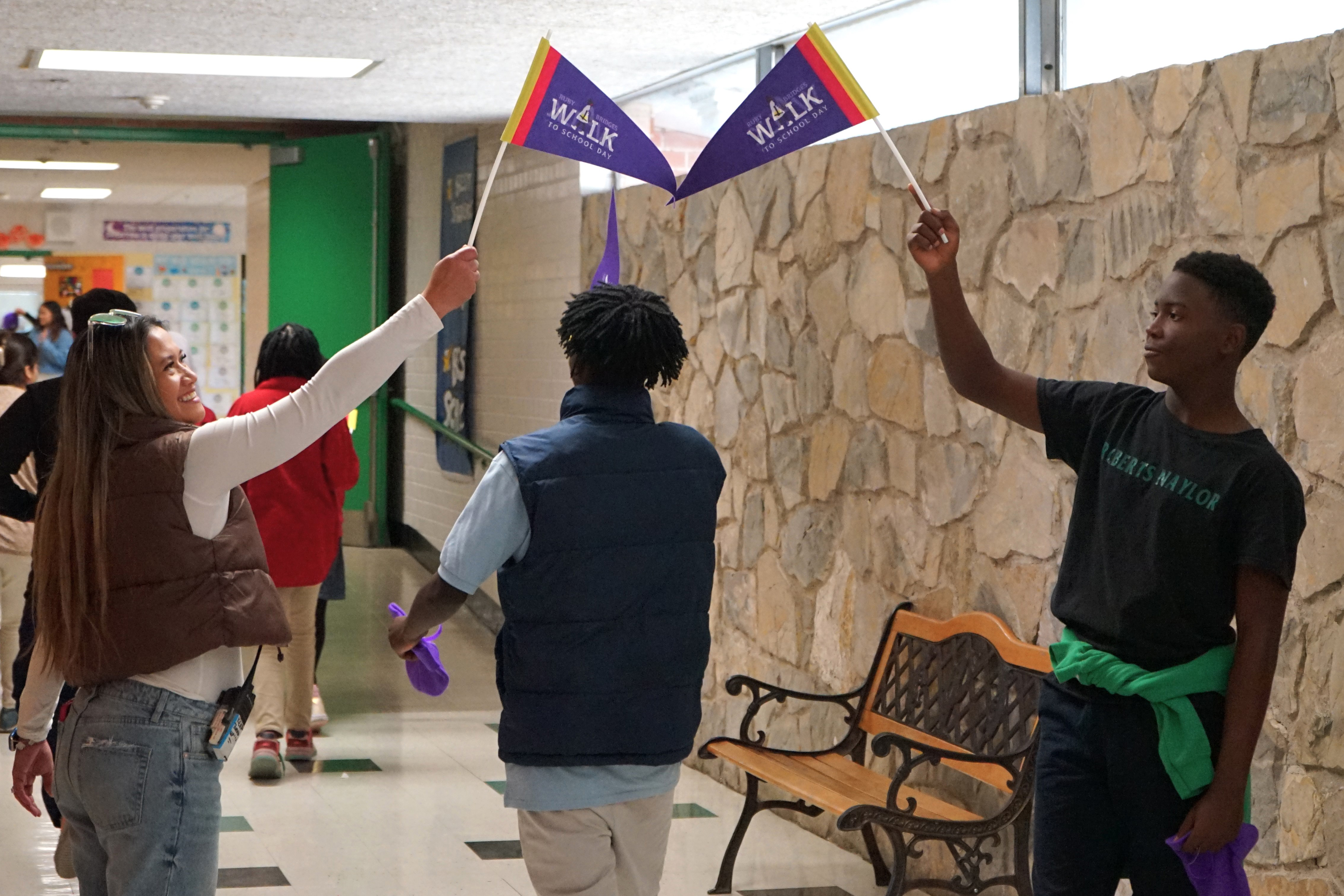 A woman and two teen boys wave purple flags above their heads in the hallway