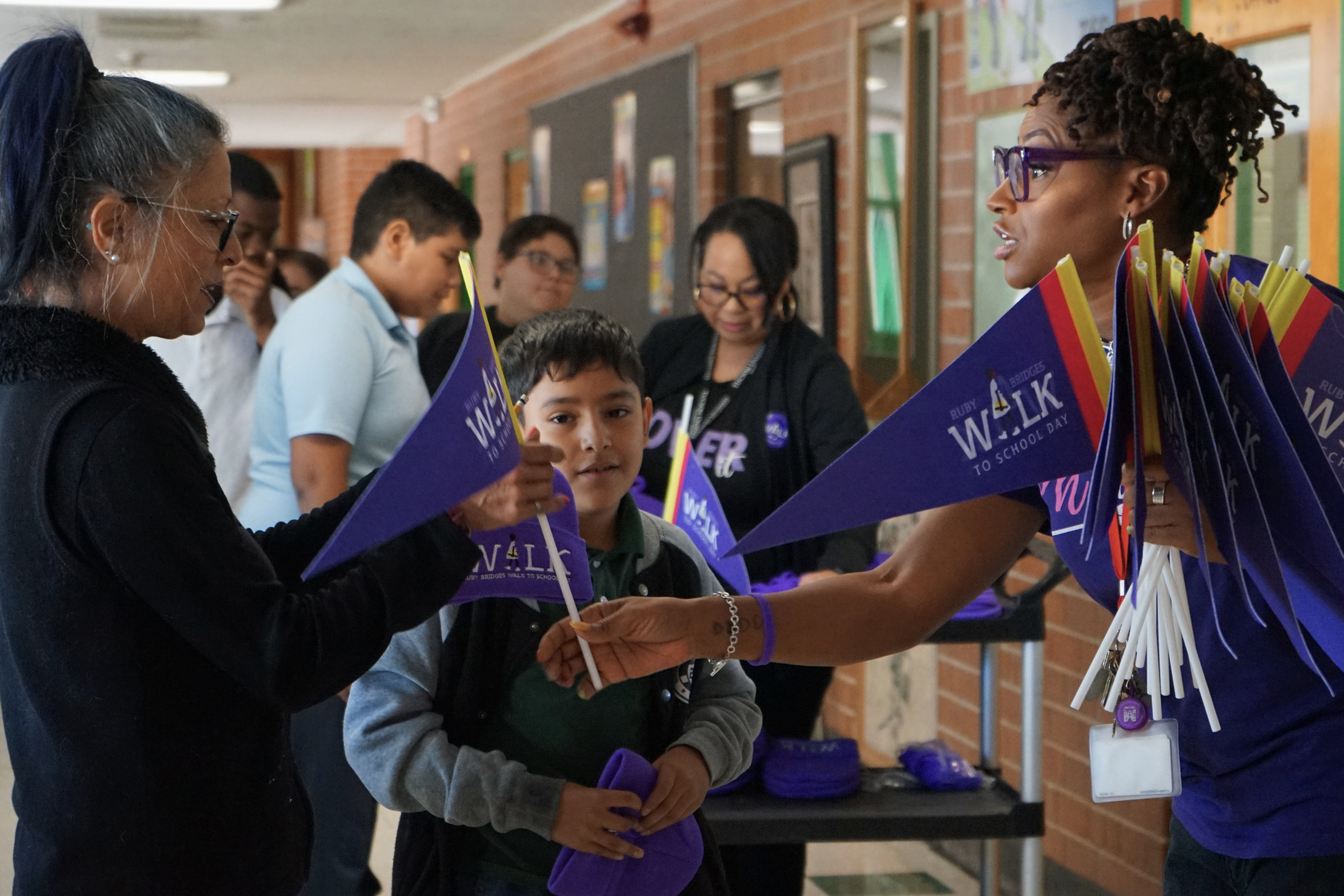 A woman in a purple shirt hands out purple flags to a woman and boy