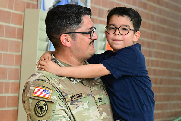 A man in a military uniform and glasses holds up his young son