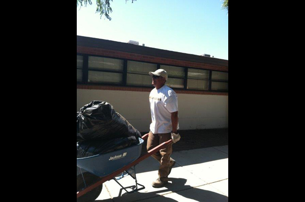 Man pushing wheelbarrow of trash outside school building