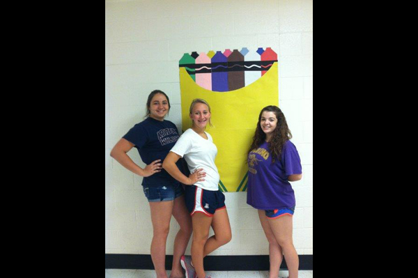 Students stand in front of a mural of crayons in the crayon box on the wall in the school hallway