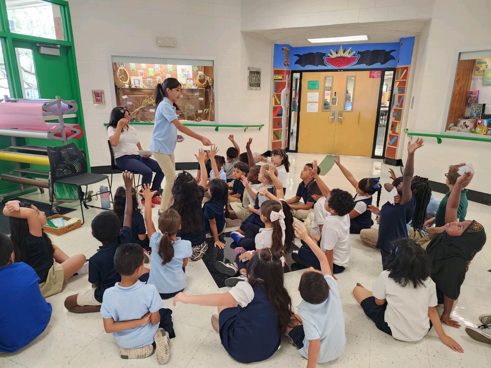 Students sit on the floor of the cafeteria and raise their hands during a group activity