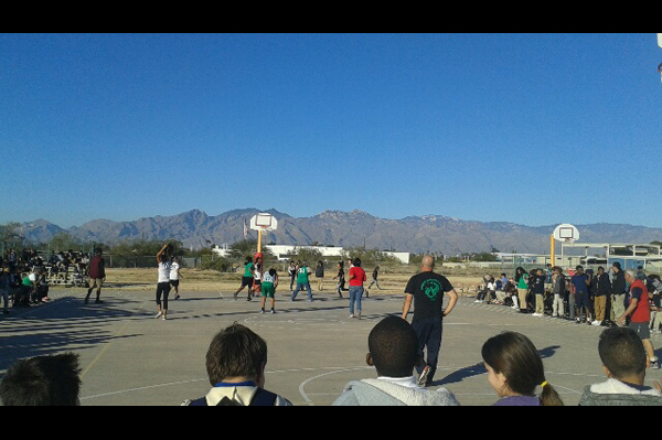 Staff and students play basketball on court while other students watch
