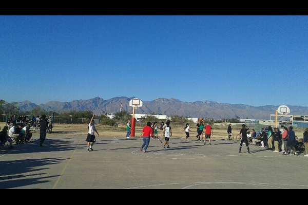 Staff and students play basketball on court while other students watch