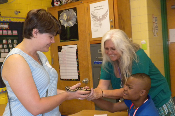 Teacher holds snake while student and teacher pet snake