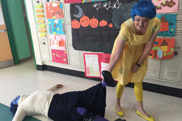 A student dressed in Halloween costume pretends to drag another student dressed in Halloween costume on the floor 