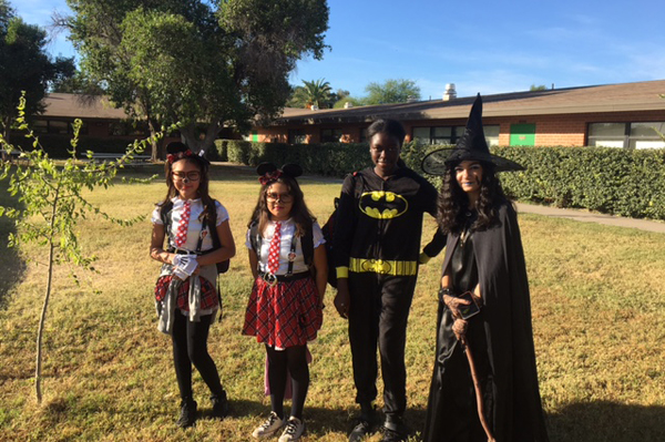 4 students dressed in Halloween costumes stand outside of school building