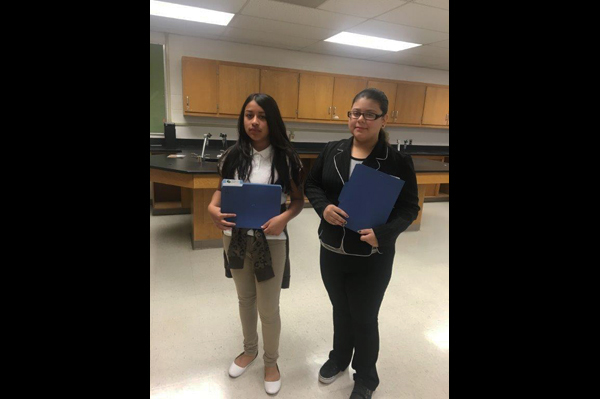 2 Students holding folders standing in classroom
