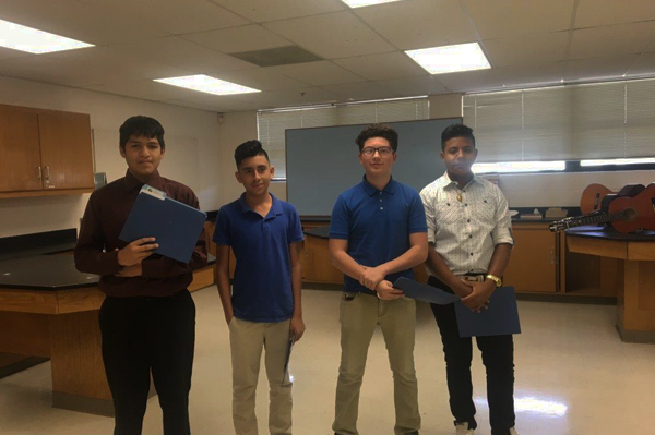4 students holding folders standing in classroom