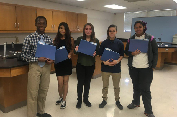 5 students holding folders standing in classroom