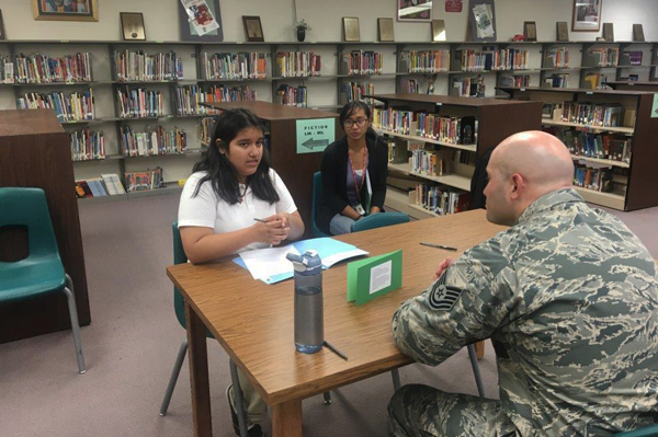 students sitting at table talking with soldier