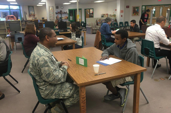 Student sitting at table talking with soldier while other students sit at other tables talking with professionals