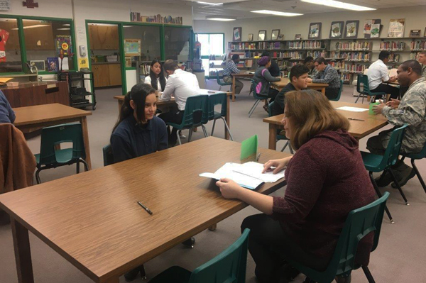 students sit at tables in library while talking to professionals