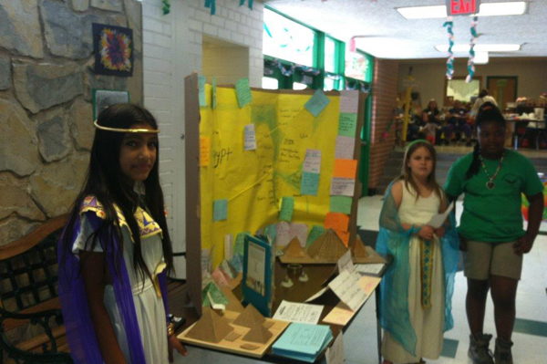 Students dressed in traditional heritage clothing standing in front of project display in school hallway